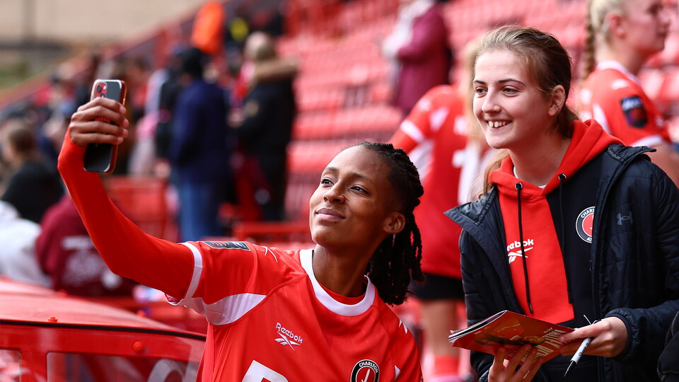 Elisha N'Dow in red takes selfie with fan in red and black at stadium